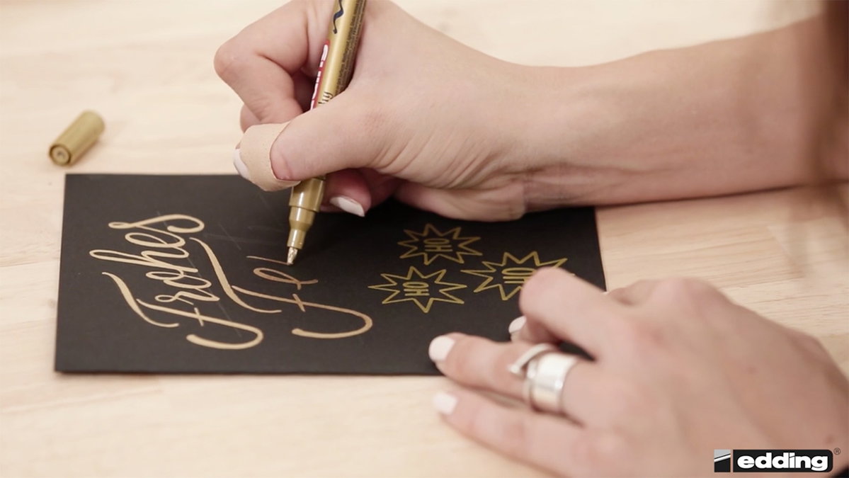 Dann malt Hannah die Buchstaben mit einem speziellen edding-Stift nach und verziert ihre Karte noch mit süßen Sternen.