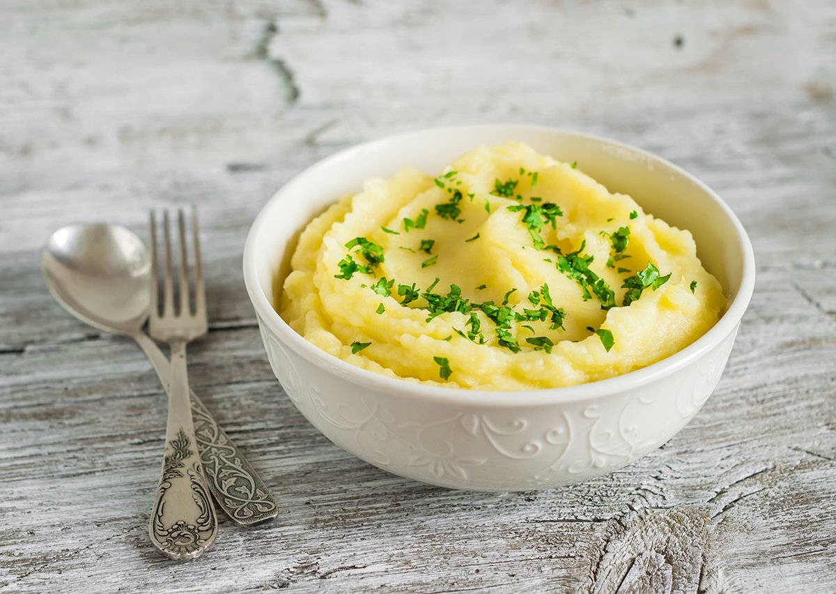 In einer Porzellanschüssel angerichtetes Kartoffelpüree auf einem rustikalen Holztisch