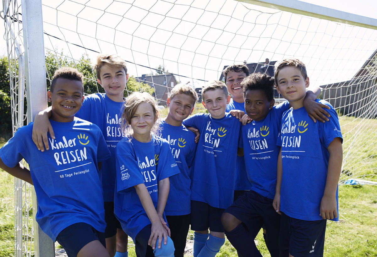 Acht Kinder in blauen T-Shirts mit der Aufschrift Kinderreisen vor einem Fußballtor