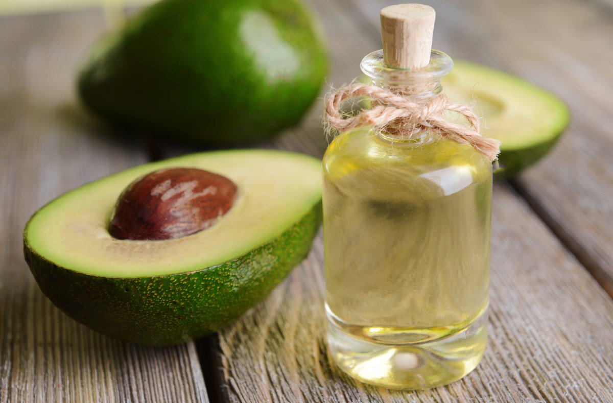 Ein Glas mit Avocado-Öl vor einer frischen, halbierten Avocado