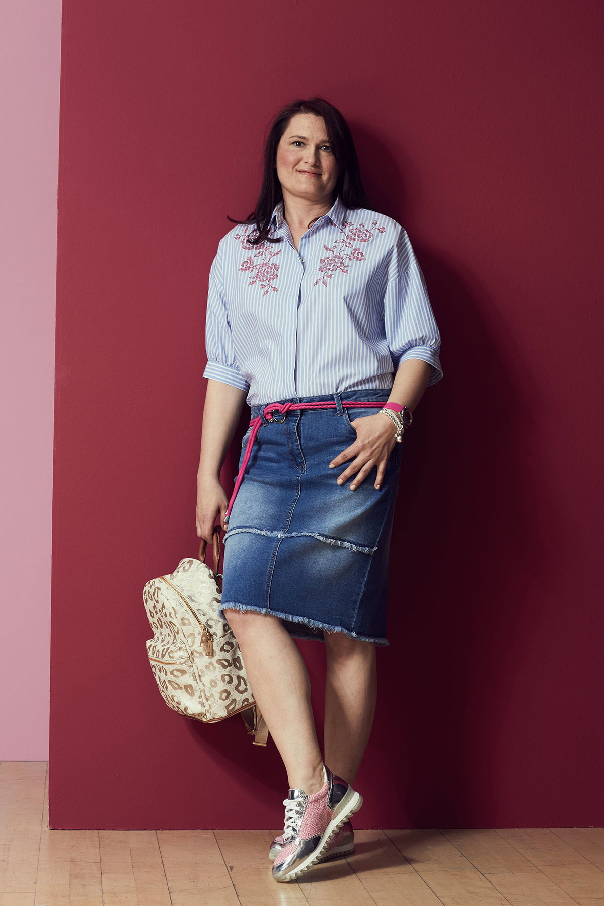 Inga lehnt an einer Wand und trägt eine gestreifte Bluse mit Stickerei zu Jeansrock und Turnschuhen