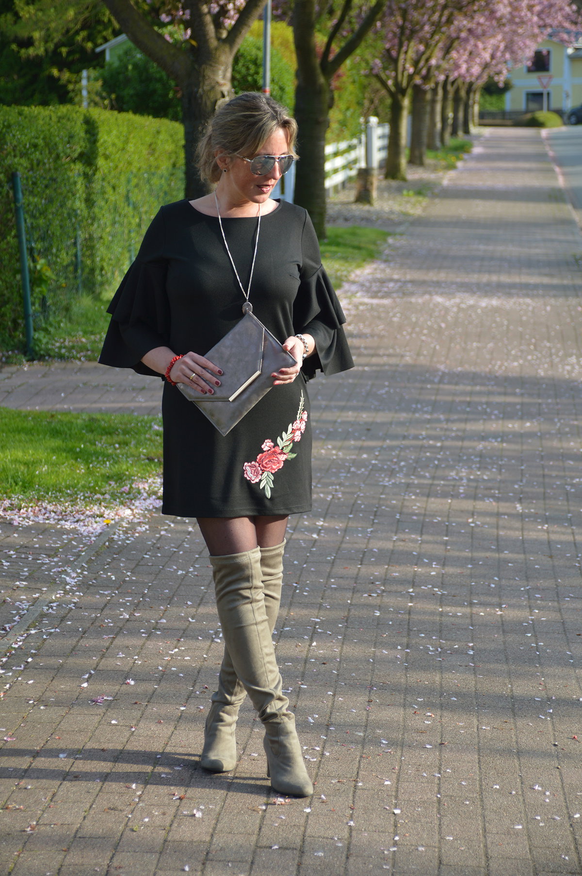 Attraktive Frau mittleren Alters in schwarzem Blumenkleid und Overknee-Stiefeln