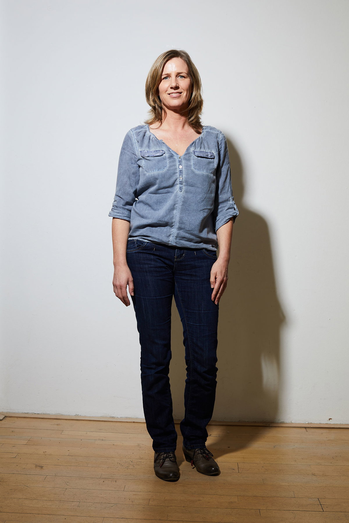 Anja vorher in Jeans und blauer Bluse mit schulterlangen Haaren.