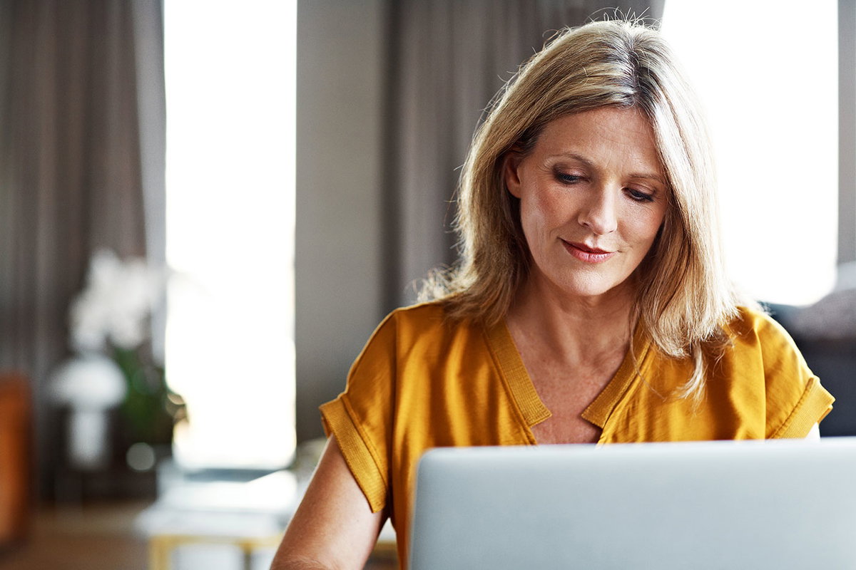 Blonde Frau mittleren Alters sieht versonnen auf den Laptop-Bildschirm