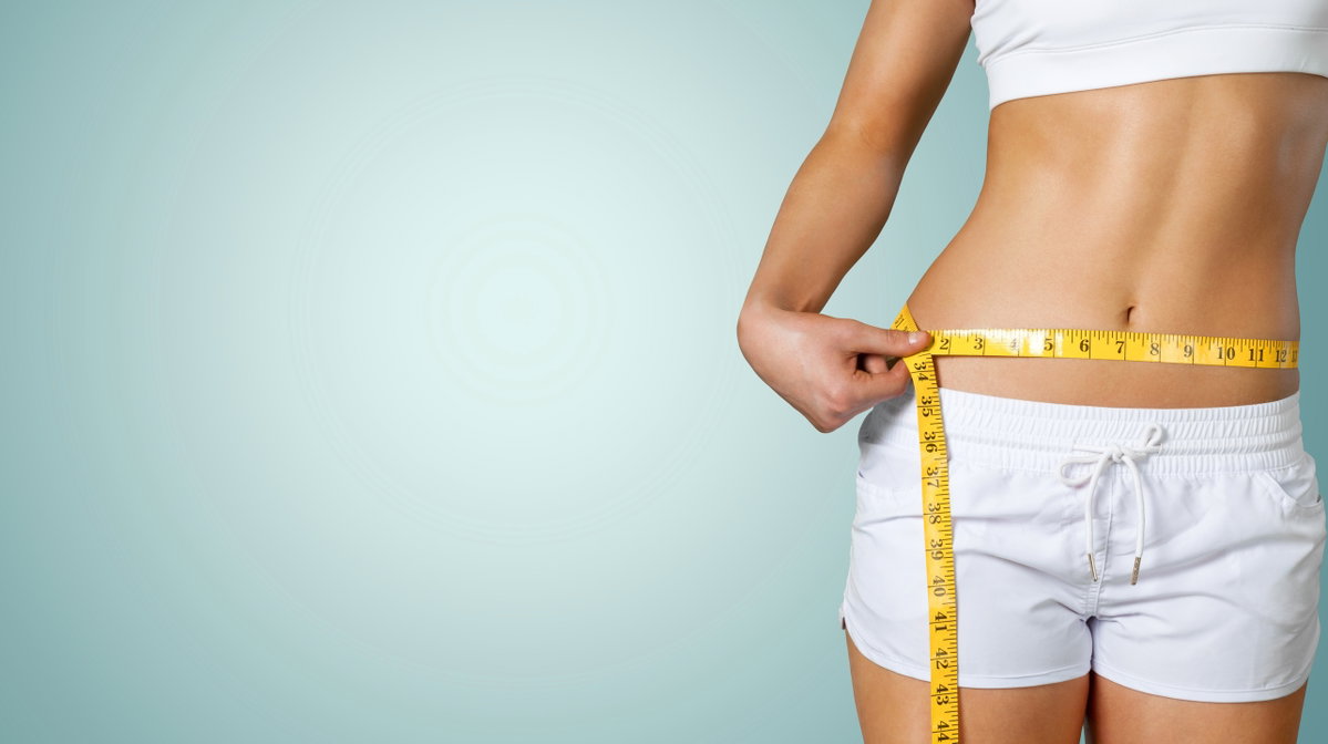 Leicht bekleidete Frau hält sich ein Maßband um den Bauch