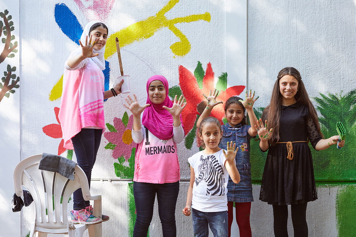 Kinder verschiedener Herkunft mit Pinseln und Farbrollen vor einer bemalten Gartenmauer