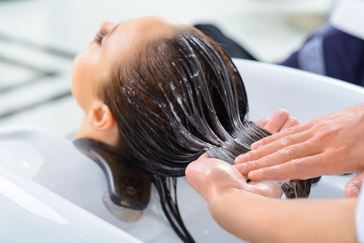 Friseur behandelt Haare einer Frau überm Waschbecken
