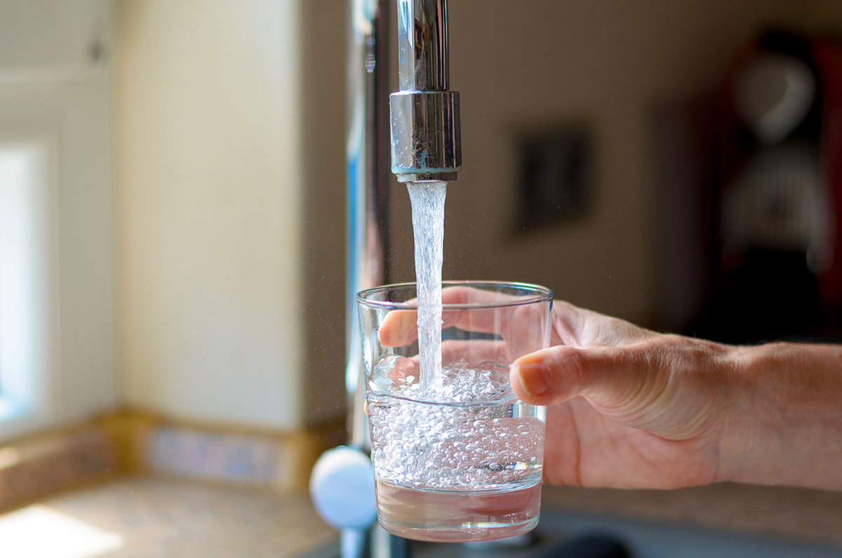 Hand hält Glas unter laufenden Wasserhahn