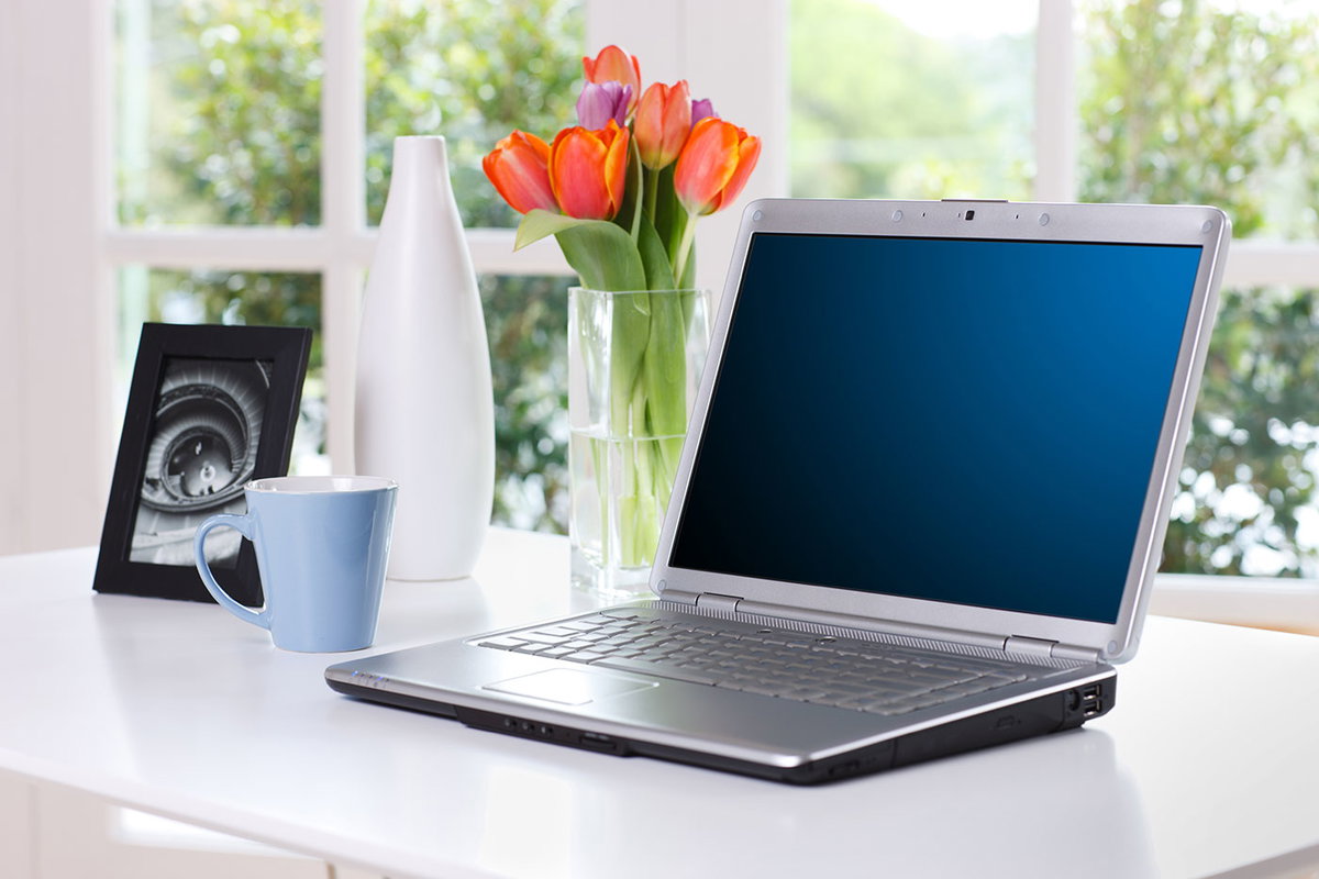 Schreibtisch mit Laptop, Tulpen, Bilderrahmen und Kaffeebecher